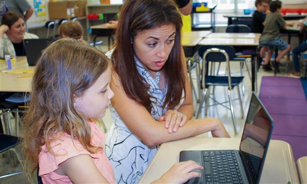 A woman works with a girl on a laptop